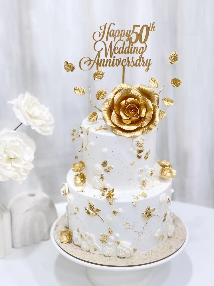 Cake dua tingkat putih dengan bunga emas untuk ulang tahun pernikahan ke-50