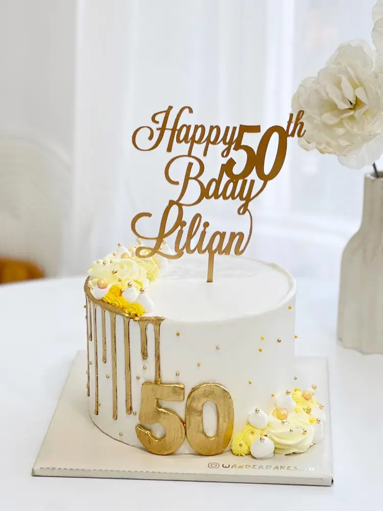 Cake putih dengan drip emas, angka 50 emas dan topper Happy 50th Bday